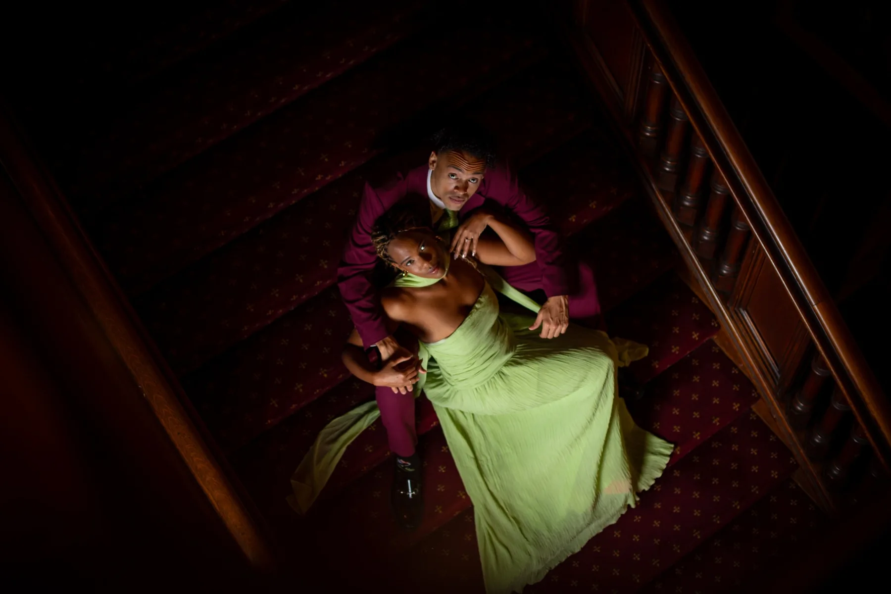 Overhead view of Alexis and Gary embracing on the burgundy-carpeted staircase