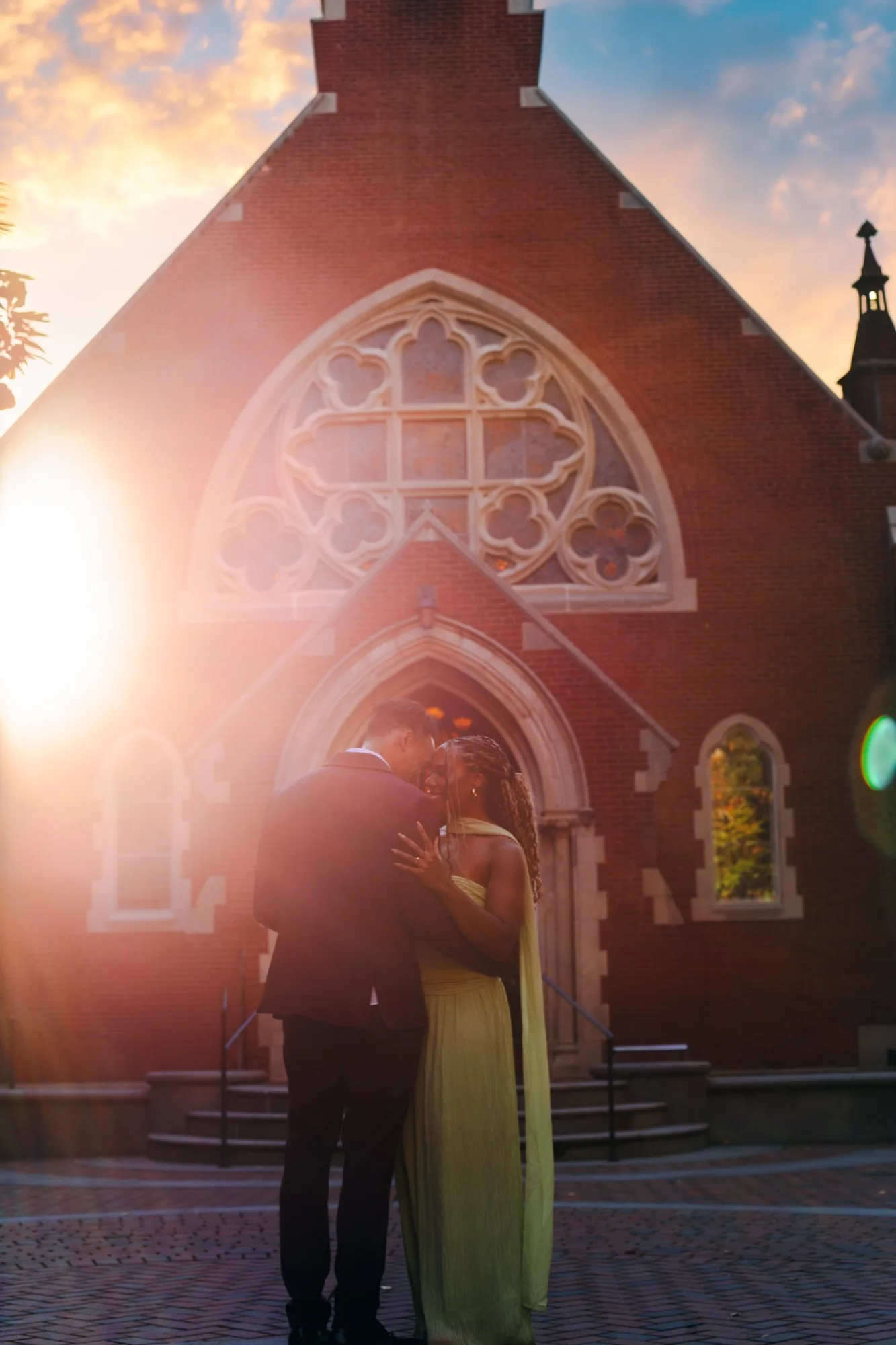 Alexis and Gary embracing in front of a historic church at sunset