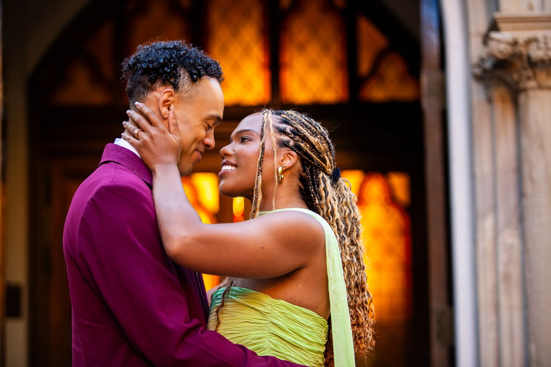 Alexis and Gary embracing in front of warm golden architectural windows